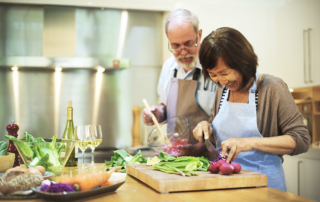 Senior couple cooking and cutting vegetables in kitchen