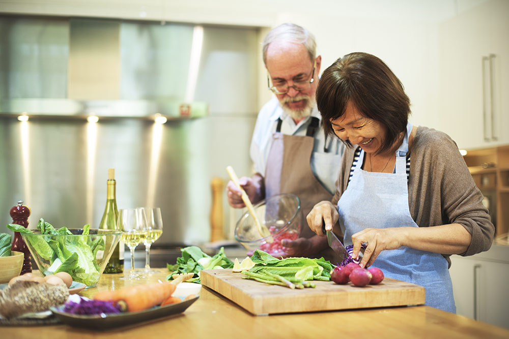 Senior couple cooking and cutting vegetables in kitchen