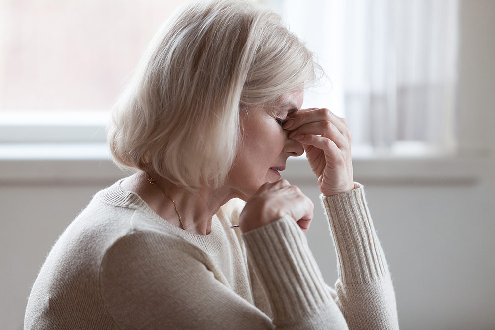 Senior woman dizzy lightheaded grabbing top of nose by head worried