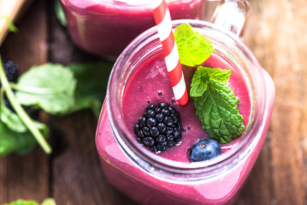 Close up image of mason jar with blueberry smoothie with blueberry, blackberry and mint on top
