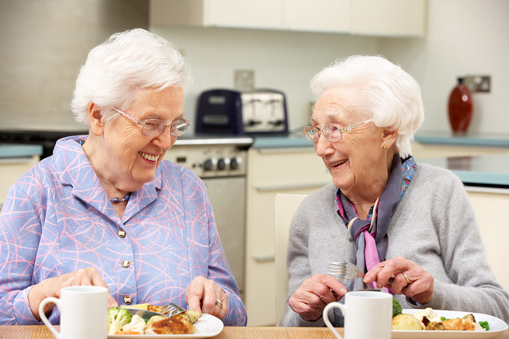 Two senior women sitting at a table eating dinner
