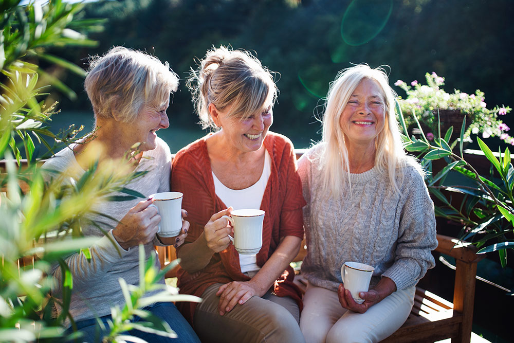 Small group of senior women smiling and drinking coffee while talking outside at independent living community