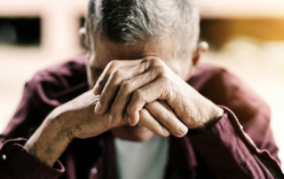 Depressed senior man with head in hands looking down