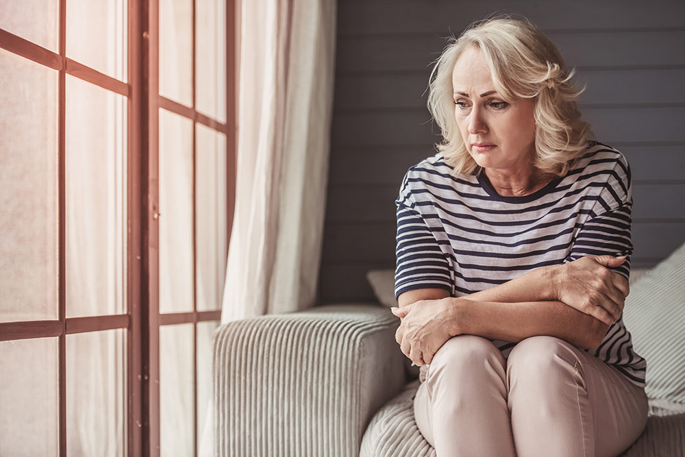 Depressed senior woman sitting on couch with arms crossed