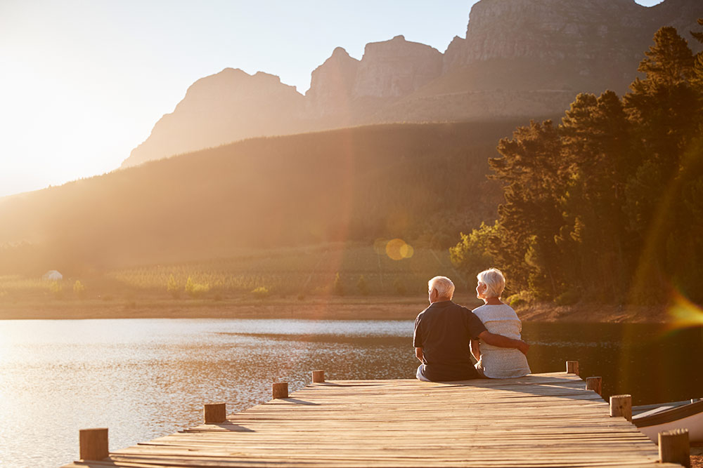 Senior couple enjoying retirement sitting on the dock at a lake at sunset