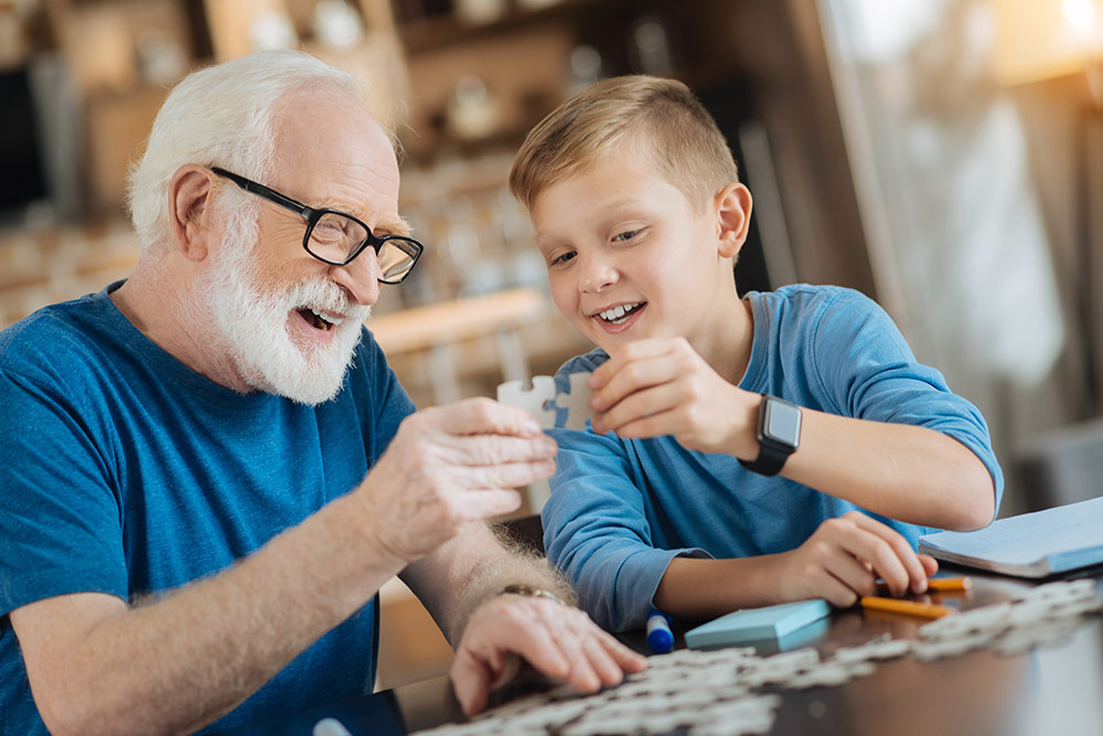 Senior man with grandson playing with puzzle pieces