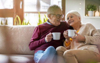 Senior couple sitting on couch drinking coffee happy, retired