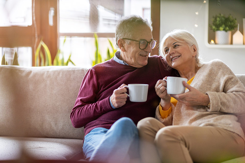 Senior couple sitting on couch drinking coffee happy, retired