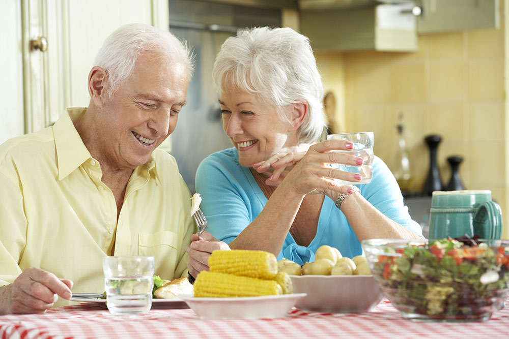 Senior couple sitting together, laughing and eating dinner
