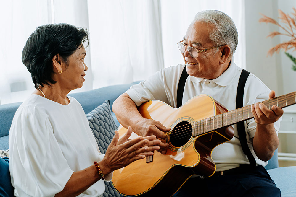 Senior couple sitting on couch, senior man playing guitar