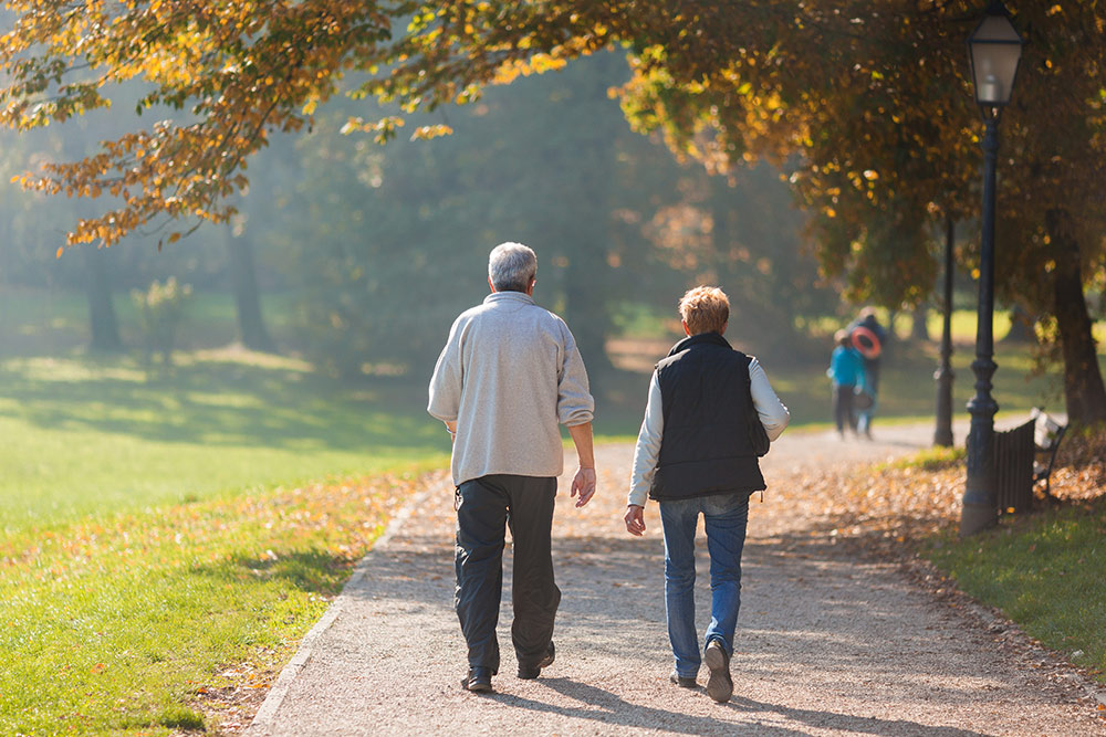 Senior man and woman walking outside on path in a park in fall