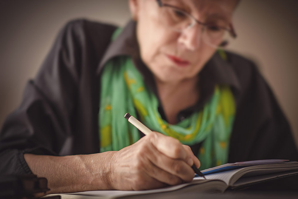Senior woman writing in journal, sitting at table, mindfulness journaling